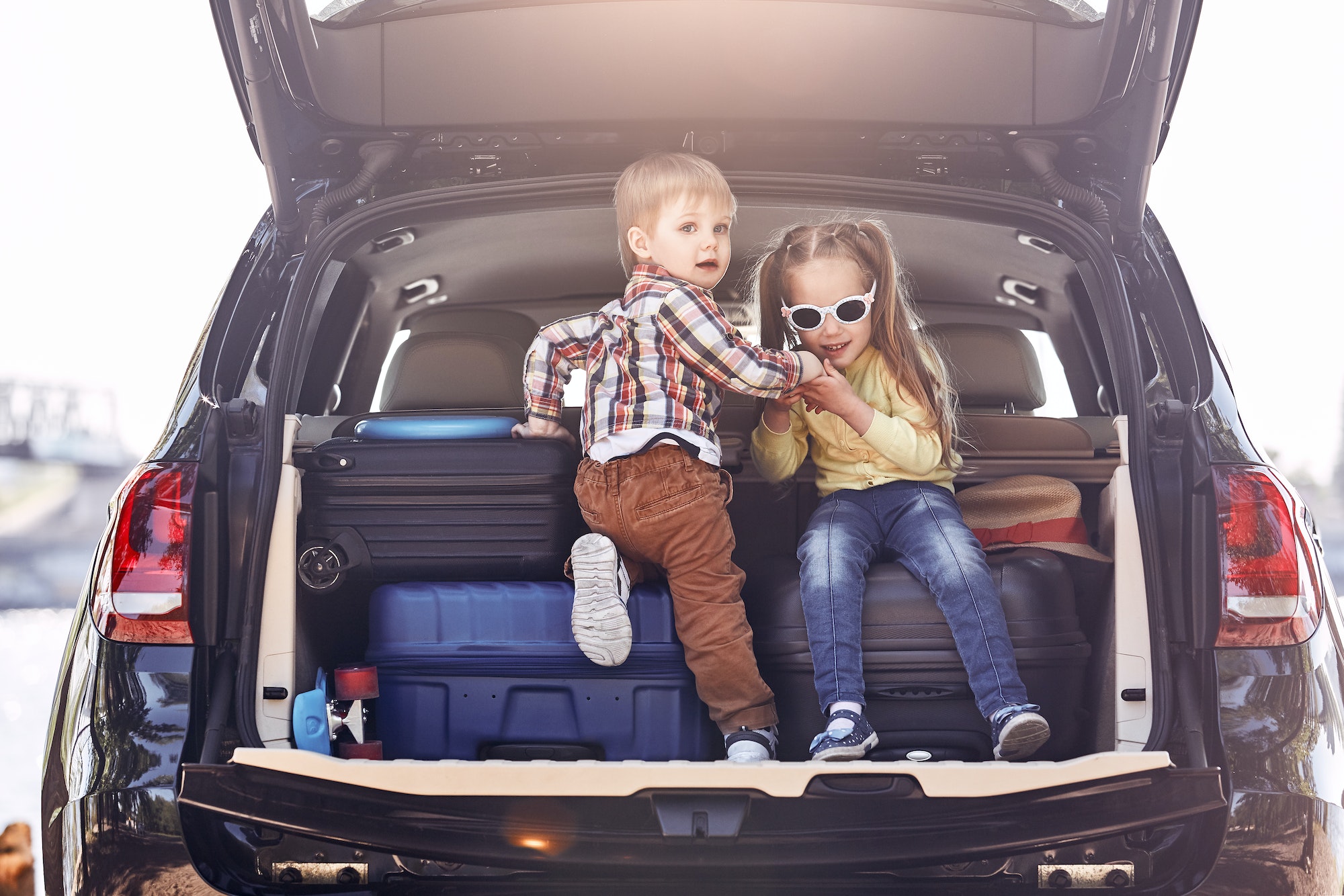 Beginning of the trip. Little cute kids in the trunk of a car with suitcases. Family road trip
